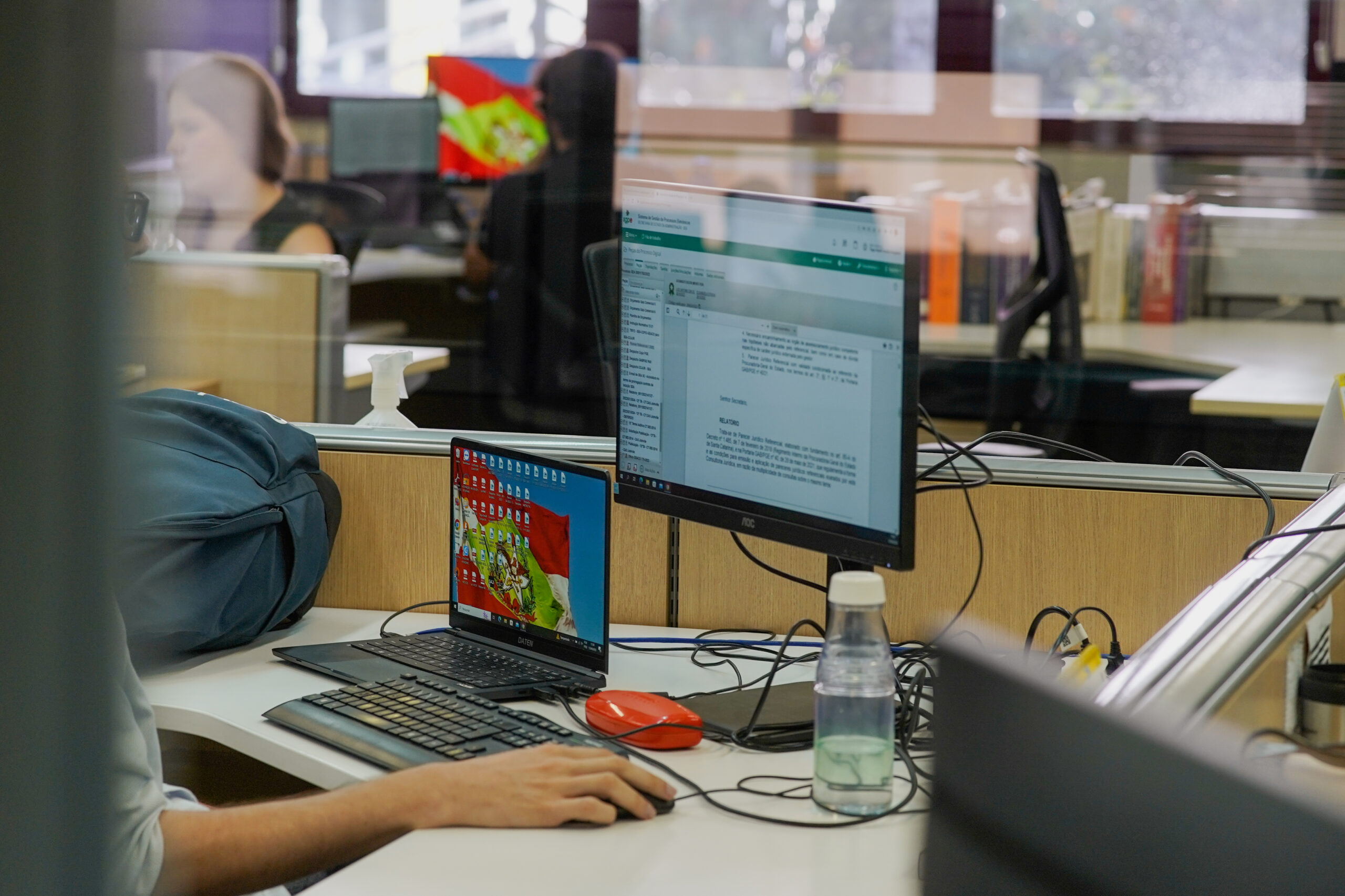 Servidor trabalhando no computador e monitor de computador com fundo da bandeira do Estado.